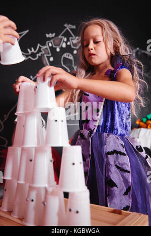 Girl in witch costume arranging pyramid of plastic cup Stock Photo