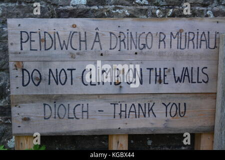 Handwritten outdoor warning sign in permanent marker  in welsh and english language on wooden boards re do not climb on walls at ancient ruins UK Stock Photo