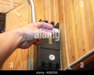 Male hand next to a main switch box hanging on the wooden wall, closeup indoor shot Stock Photo