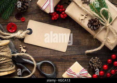 Christmas setting - xmas gift wrapped in kraft paper, burlap twine, vintage scissors, red buttons, reindeer, fir branches and pine cones and an empty  Stock Photo