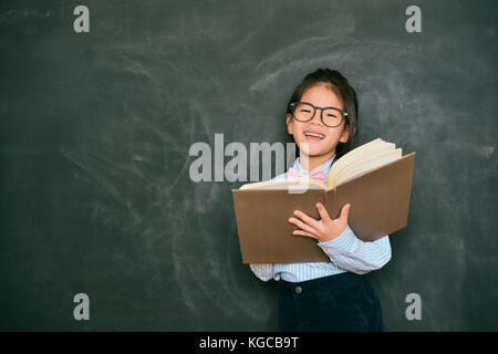 happy sweet little english teacher using study book teaching student during school class and standing in blackboard background. Stock Photo
