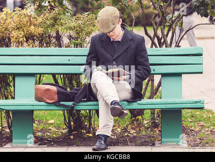 Young man sitting on the bench in a park and reading a book in Vilnius, Lithuania Stock Photo