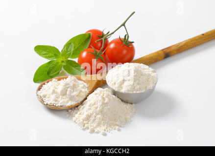 wheat flour on wooden spoon and in metal bowl, ripe tomatoes and fresh basil on white background Stock Photo