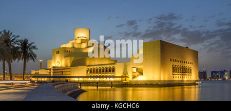 Museum of Islamic Art, Doha, Qatar at night exterior view with light reflection in the Arabic gulf with trees and skyscrapers in the background. Stock Photo