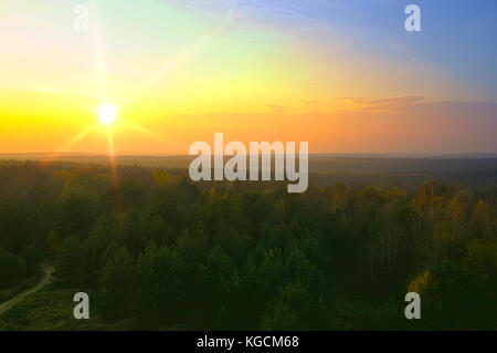 Yellow sunset over wide horizon with forest and dirty road. Golden autumn rural scene. Stock Photo