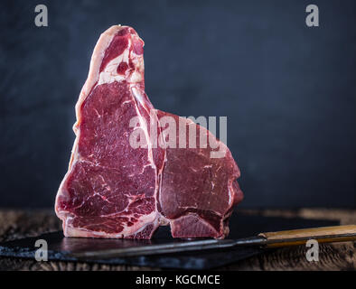 Beef steak T-bone. Raw beef steak T-bone on slate board with butcher and fork. Stock Photo