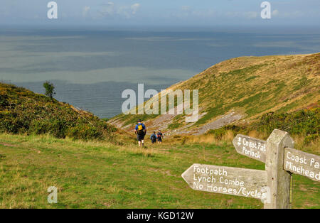 Walkers on the South West Coast path, from Minehead to Porlock.Sign post points down a stony combe towards the sea.Somerset. UK. Stock Photo
