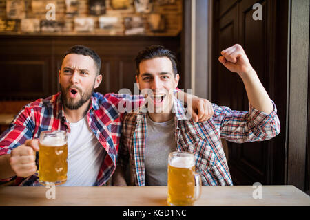 Three men with beer rejoice the victory of their favorite team in the pub Stock Photo