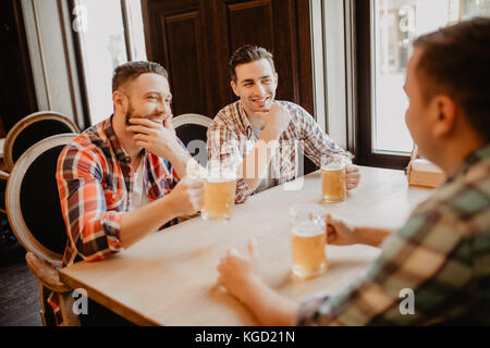 Cheerful old friends having fun and drinking draft beer in pub. Stock Photo