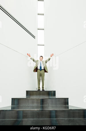 A businessman atop a series of steps celebrating. Stock Photo