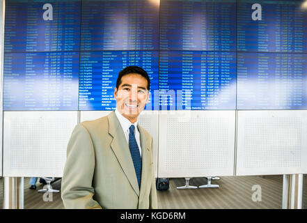Portrait of a happy businessman in an airport in front of the electronic departures board. Stock Photo