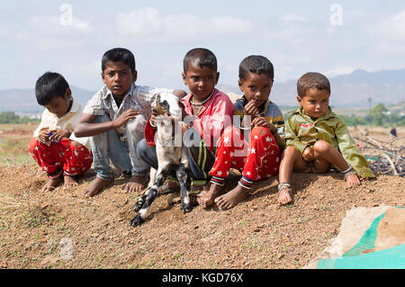 Goat herder kids sitting and holding a baby goat, Pune, Maharashtra Stock Photo