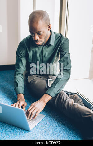 Young afro businessman sitting using notebook tapping keyboard and tablet hand hold - business, technology, multitasking Stock Photo