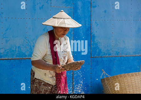 Burmese woman wearing traditional bamboo hat sifting food in village along Inle Lake, Nyaungshwe, Shan State, Myanmar / Burma Stock Photo