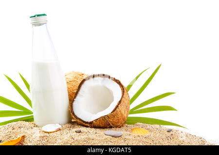 Fresh cut in half coconuts with coconut milk in bottle on tropic beach sand isolated on white background. Stock Photo
