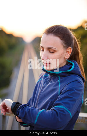 Portrait of young sporty woman checking heart rate on fitness watch. Athletic girl standing outdoor after fitness training Stock Photo