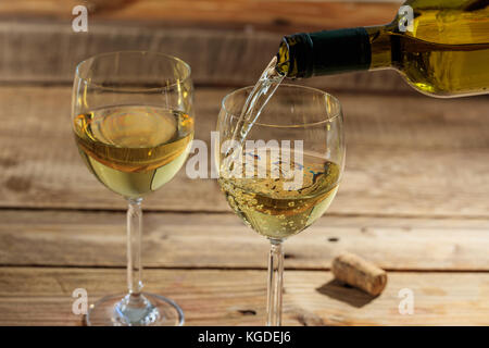 Pouring white wine in a glass on a wooden table Stock Photo