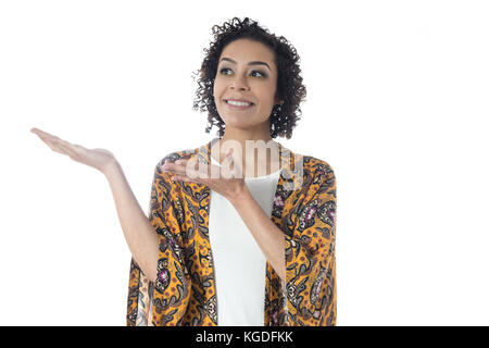 Beautiful slim girl is smiling and gesturing with her hands. She holds something out with her hands. Short and curly haired woman wears yellow clothes Stock Photo