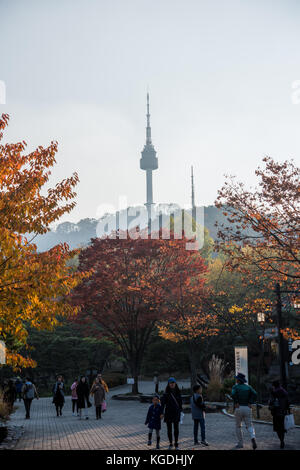 Autumn coloured trees with korean people in the foreground and a view of Seoul N Tower in the background Stock Photo