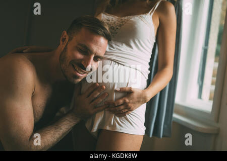 Happy pregnant woman enjoying with husband in bedroom Stock Photo