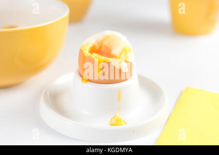 Close up of soft-boiled egg with cracked eggshell for breakfast next to yellow tableware set Stock Photo