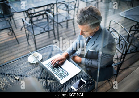 Mature businessman with laptop outside a cafe. Stock Photo