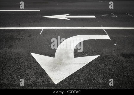 Turn or go straight street signs on asphalt, arrow pointing at viewer, conceptual background with focus on the first arrow. Stock Photo