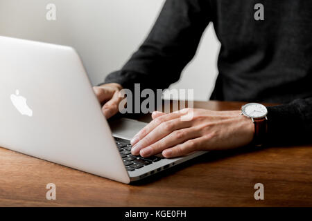 Styled lifestyle stock minimalist photo of a man working/typing on a laptop at a wooden desk. Stock Photo