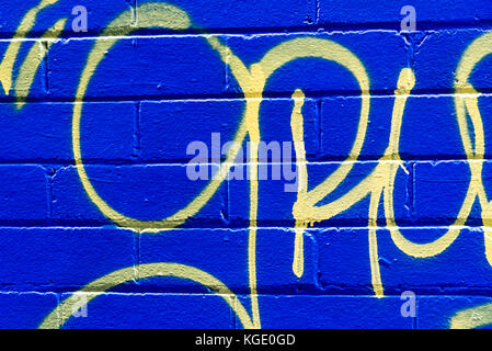Grunge blue brick background with abstract yellow pattern. Urban street art texture wall, yellow cursive marking painted on blue. Stock Photo