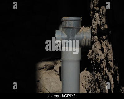 Plastic sewer pipe with a triple adjustable, illuminated sun, against clay wall and darkness, an empty space for text from the top left. Stock Photo