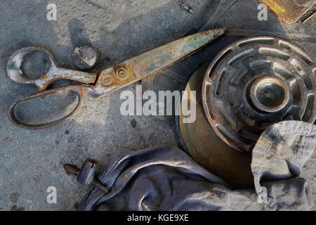 Vintage metal rusty scissors lie on asphalt, near the metal wheel and old rags, street still life from old objects. Stock Photo