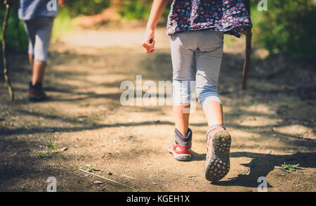 Children hiking in mountains or forest with sport hiking shoes. Girls are walking trough forest path wearing mountain boots and walking sticks. Frog p Stock Photo