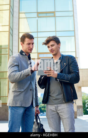 Portrait of two handsome men using digital tablet together standing outside of modern office building Stock Photo