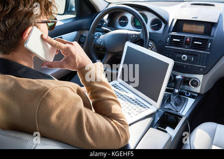 Rear view of unrecognizable successful man using laptop and speaking by phone sitting inside of expensive car, copy space Stock Photo