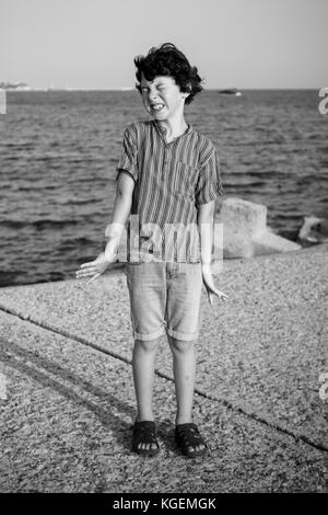 A disgruntled boy is standing by the sea. Black and white. Stock Photo