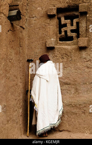 Ethiopian pilgrim is praying by the wall of church carve in solid rock in Lalibela, Ethiopia Stock Photo