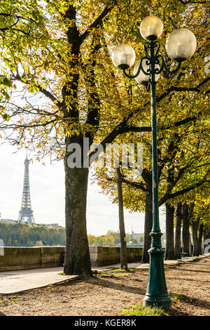 The Eiffel Tower seen between the chestnut trees planted alongside the banks of the river Seine with an old style street light in the foreground. Stock Photo