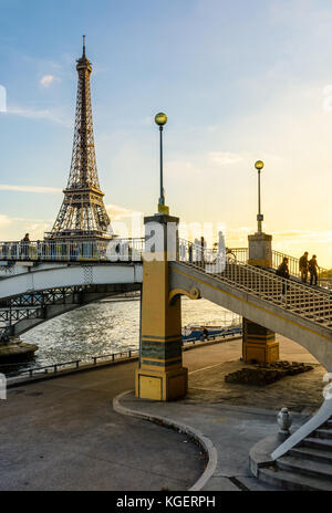 View of the Eiffel Tower at sunset with people strolling on the Debilly footbridge over the river Seine in the foreground. Stock Photo