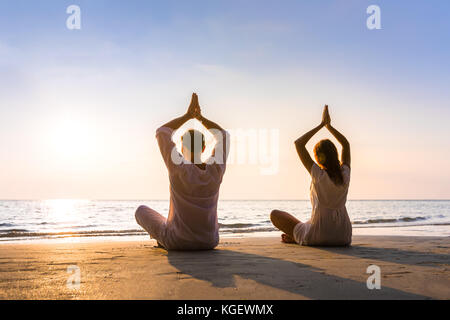 Couple practicing yoga on the beach in morning sunlight, relaxation, balance and harmony, healthy lifestyle Stock Photo