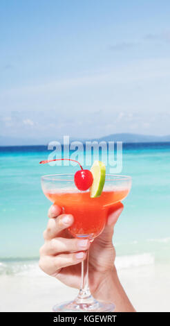 Strawberry Daiquiri cocktail in woman's hand at the beach restaurant over beautiful blue sea and sky background Stock Photo