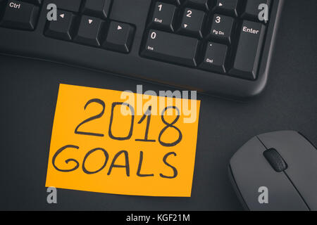 2018 Goals. Paper note with writing 2018 Goals on a desk with black keyboard and grey wireless mouse. Close up. Stock Photo