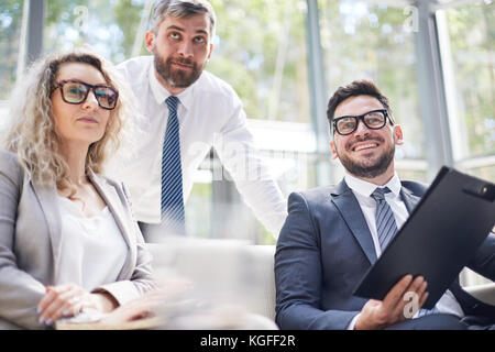 Talented group of managers in formalwear looking away with interest while having productive working meeting at modern boardroom, panoramic windows on  Stock Photo