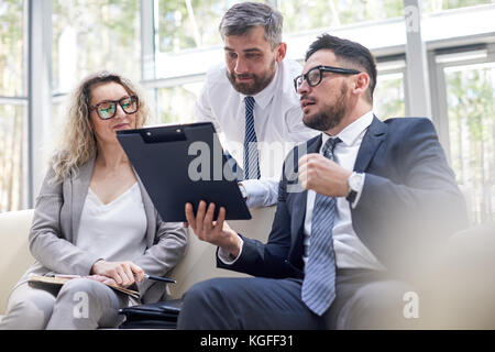 Hard-working team of managers brainstorming on joint project while having working meeting at spacious boardroom with panoramic windows Stock Photo