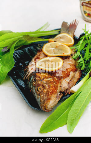 Baked carp marinated in lemon and spices with green leaf lettuce on a light background . Stock Photo