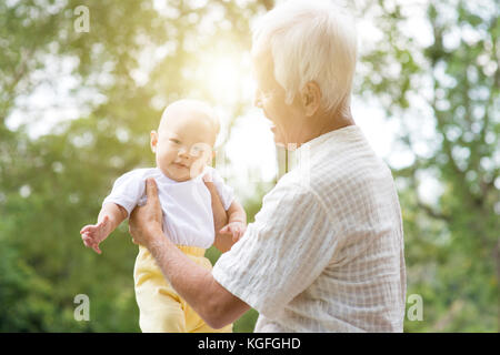 Grandfather taking care of baby grandchild in outdoor park. Asian family, life insurance concept. Stock Photo