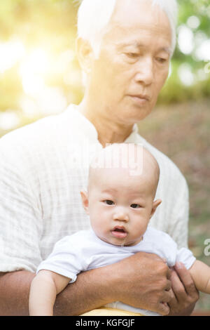 Grandfather taking care of baby grandson in outdoor park. Asian family, life insurance concept. Stock Photo
