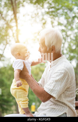 Grandfather taking care of baby grandson in outdoor park. Asian family. Stock Photo