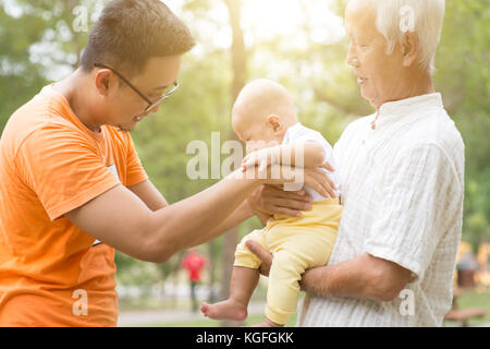 Grandfather and father taking care of baby grandson at outdoor park. Asian multi generations family. Stock Photo
