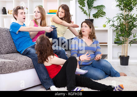 Young boy  switches the channel on TV, unsatisfied girls watching  him Stock Photo