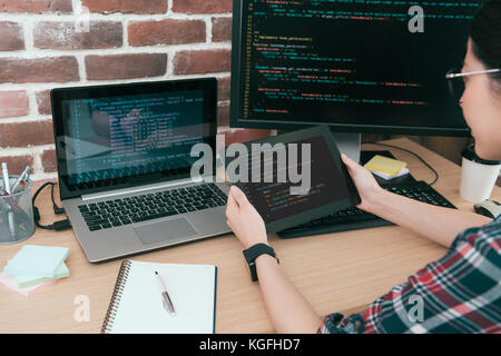 young pretty female programmer looking at mobile digital tablet pad supervising company online website security and using code data design system. Stock Photo